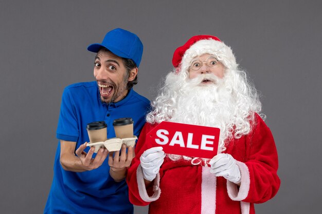 Front view of santa claus with male courier holding sale writing and coffee on grey wall