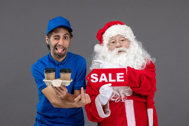 Front view of santa claus with male courier holding sale writing and coffee on the grey wall