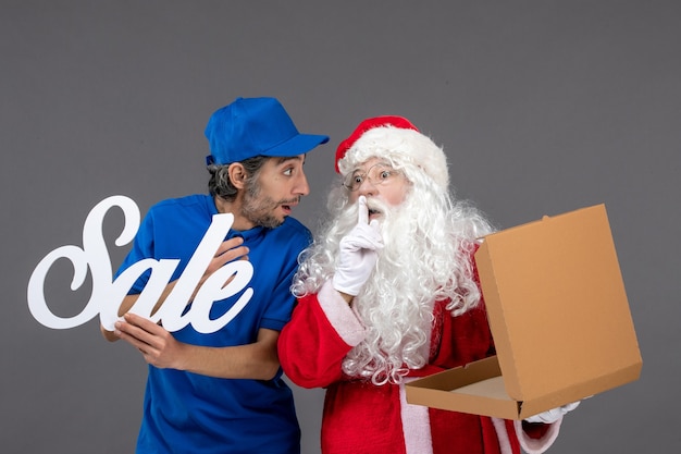 Free photo front view of santa claus with male courier holding sale writing and empty food box on grey wall