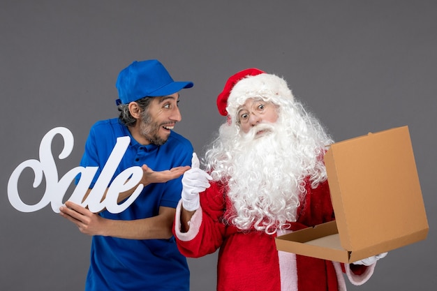 Free Photo front view of santa claus with male courier holding sale writing and empty food box on grey wall