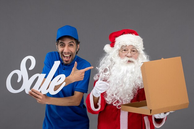 Front view of santa claus with male courier holding sale writing and empty food box on grey wall