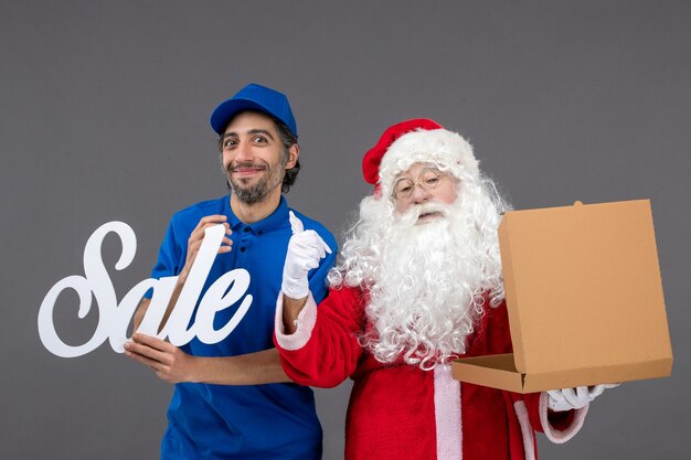 Front view of santa claus with male courier holding sale writing and empty food box on the grey wall