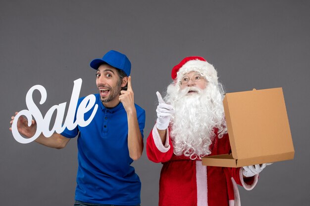 Front view of santa claus with male courier holding sale writing and food box on a grey wall