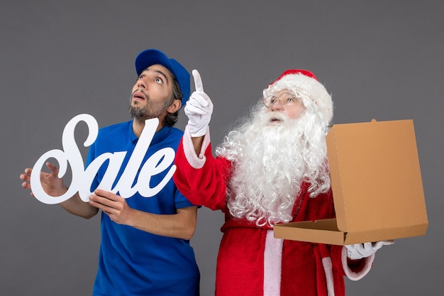 Front view of santa claus with male courier holding sale writing and food box on grey wall