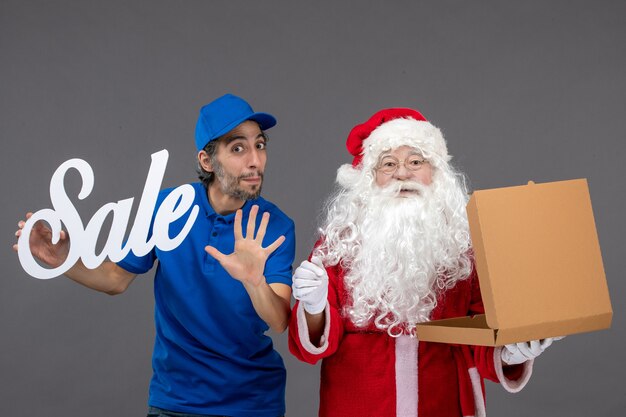 Front view of santa claus with male courier holding sale writing and food box on grey wall