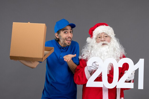 Front view of santa claus with male courier holding shopping bags and food box on grey wall