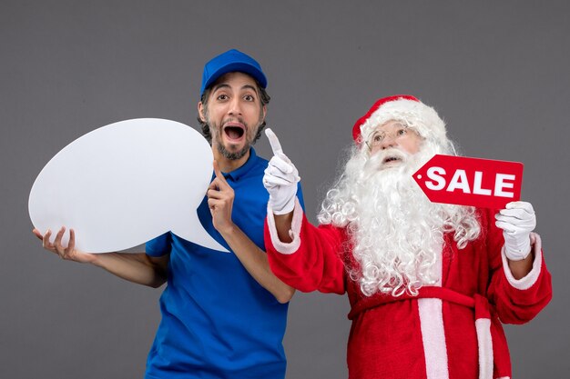 Free Photo front view of santa claus with male courier holding white sign and sale banner on the grey wall