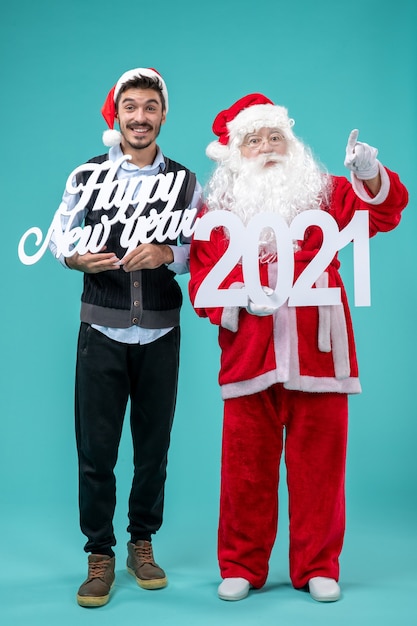 Front view of santa claus with male holding happy new year and 2021 boards on blue wall