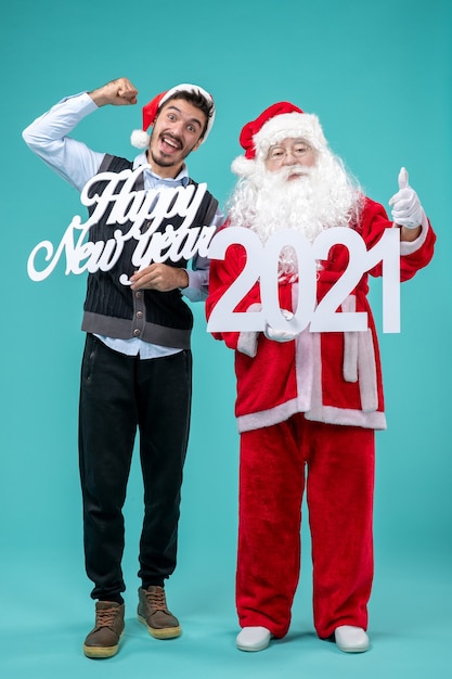 Front view of santa claus with male holding happy new year and 2021 boards on blue wall