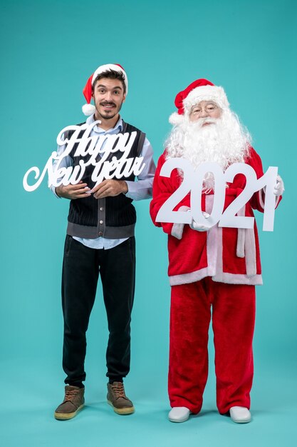 Front view of santa claus with male holding happy new year and shopping bagss on the blue wall