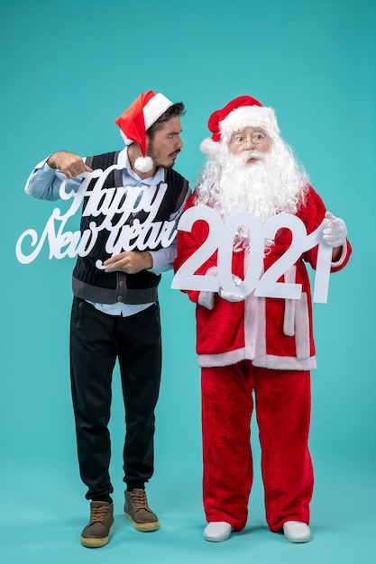 Front view of santa claus with male holding happy new year and shopping bagss on the blue wall