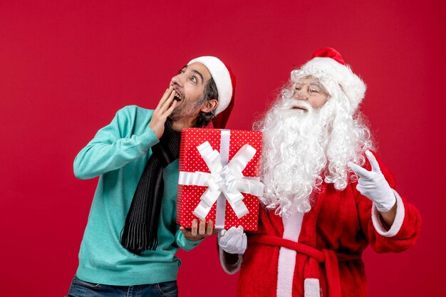 Front view santa claus with male holding holiday present on red desk gift emotion red christmas