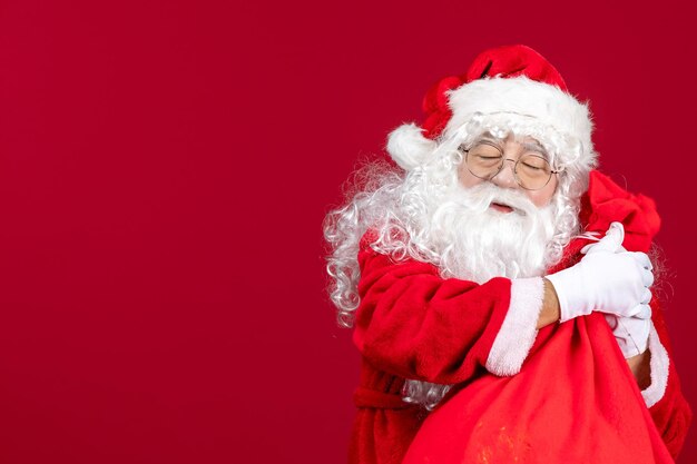 Front view santa claus with red bag full of presents for kids on red desk new year