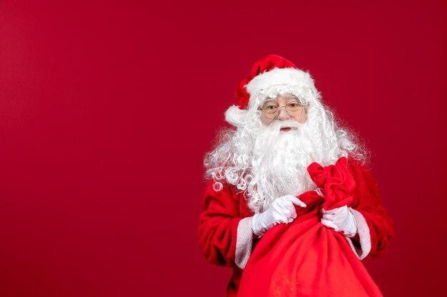 Front view santa claus with red bag full of presents on red desk new year holiday christmas emotion