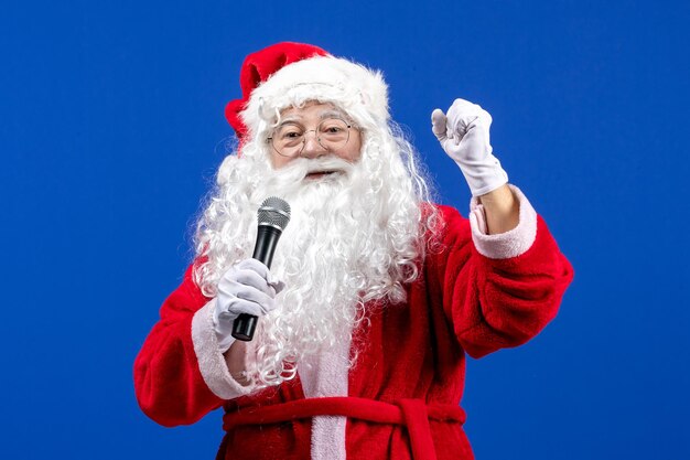 Front view santa claus with red suit and white beard holding mic on blue color new year xmas