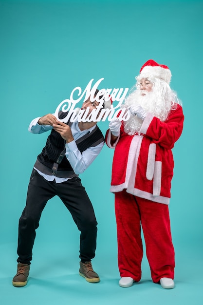 Free Photo front view santa claus with young male holding merry christmas writing on blue background