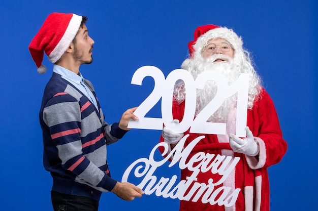 Free Photo front view santa claus with young male holding and merry christmas writings on blue new year