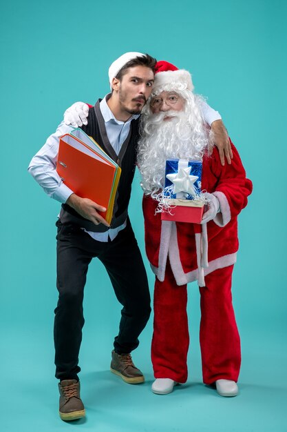 Free Photo front view of santa claus with young male and presents on blue wall