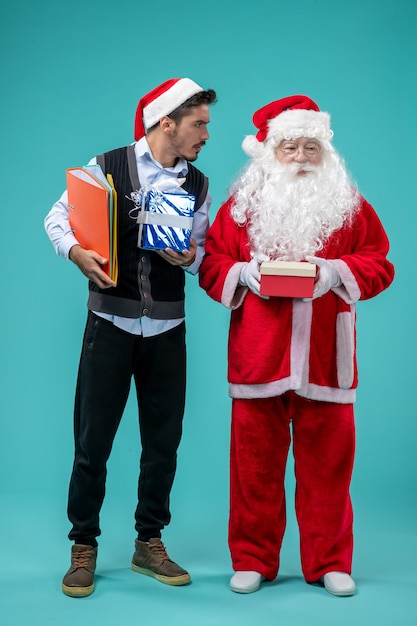 Free Photo front view of santa claus with young male and presents on blue wall