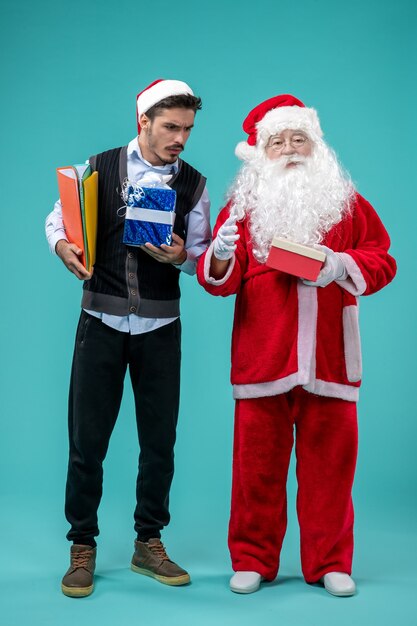 Front view of santa claus with young male and presents on blue wall