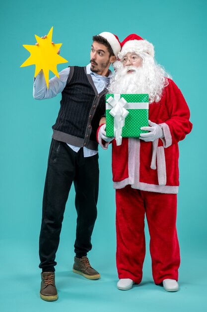 Front view santa claus with young male who's holding yellow sign on blue floor xmas new year holiday snow