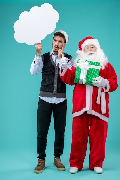 Free Photo front view santa claus with young male whos holding white cloud sign on blue floor xmas new year holiday snow