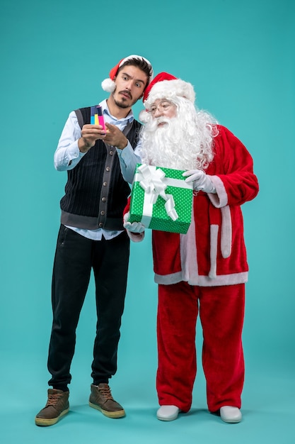 Free Photo front view of santa claus with young man and holiday present on a blue wall