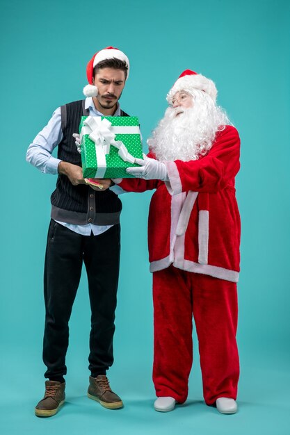 Front view of santa claus with young man and holiday present on the blue wall