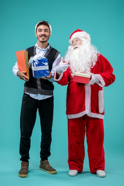 Free Photo front view of santa claus with young man and presents on a blue wall