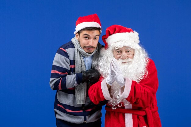 Front view of santa claus with young man shivering from cold on blue wall