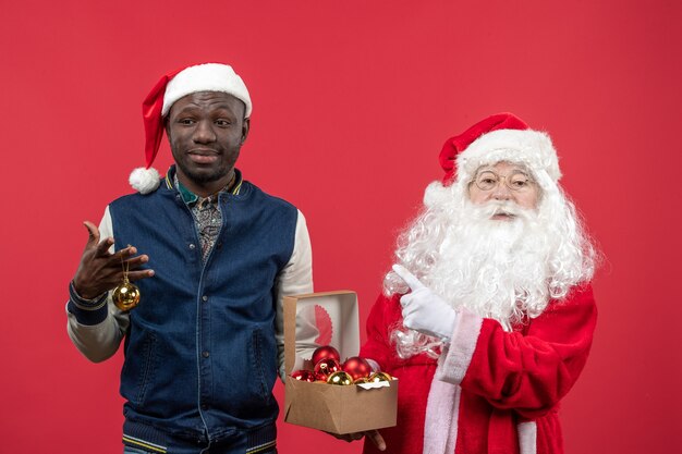 Front view of santa claus with young young man holding xmas tree toys on the red wall