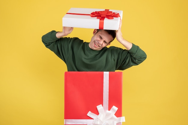 Front view scared young man standing behind big giftbox on yellow 