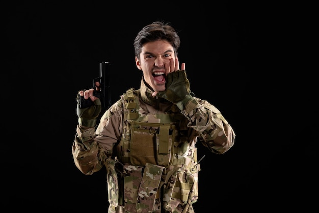 Free photo front view of screaming military serviceman in uniform with gun black wall