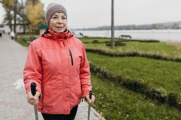 Free photo front view of senior woman outdoors with trekking sticks and copy space