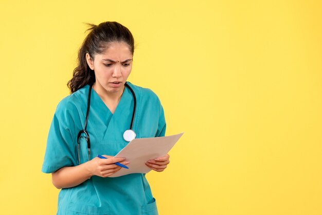 Front view serious pretty female doctor checking papers on yellow background