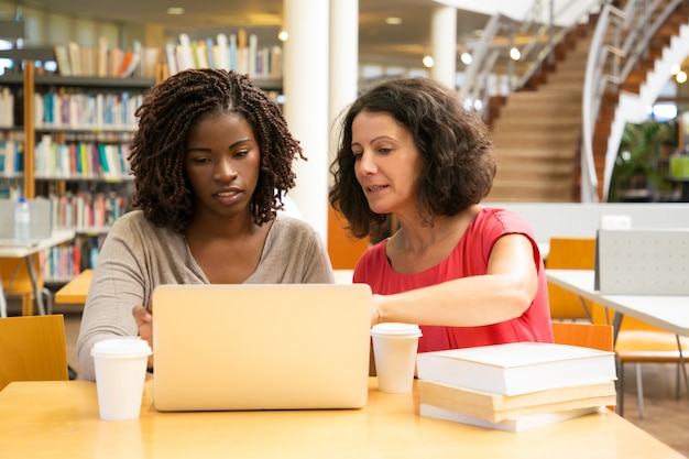 Front view of serious women sitting at table and using laptop