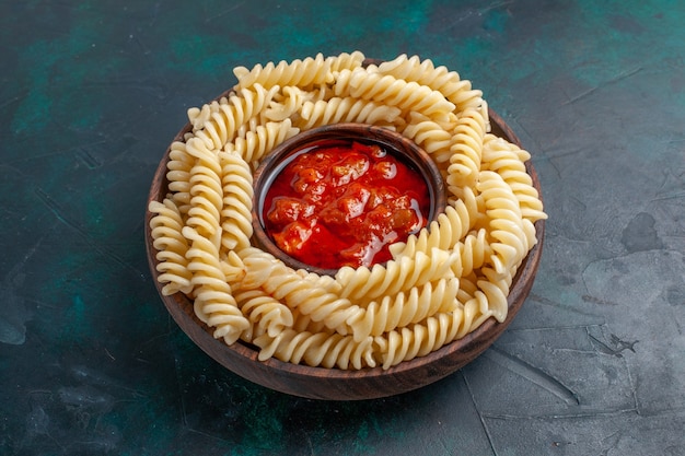 Free photo front view shaped italian pasta with tomato sauce on dark-blue surface