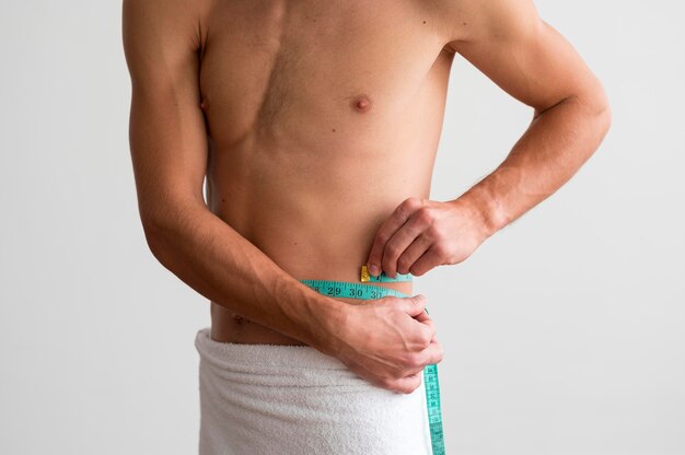 Front view of shirtless man measuring his waste with tape