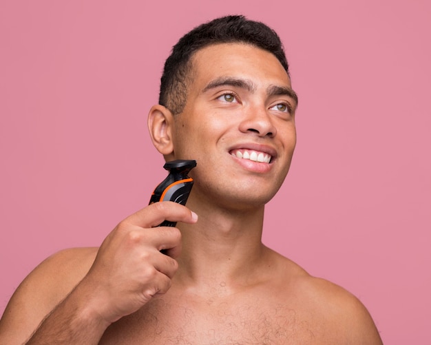 Front view of shirtless smiley man using an electric shaver