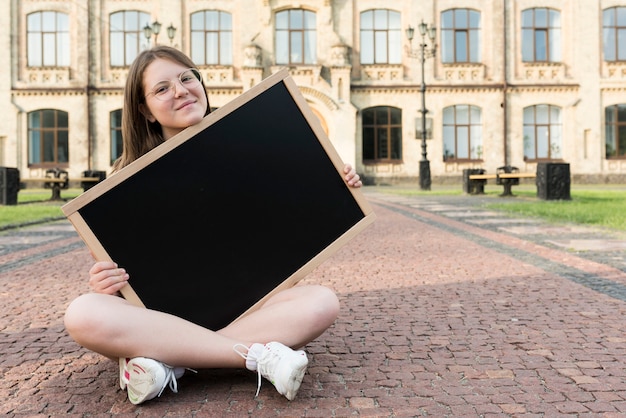 Front view sitting highschool girl holding blackboard