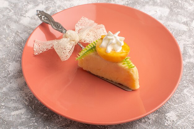 Front view slice of cake with cream and fruit slice inside peach plate on white