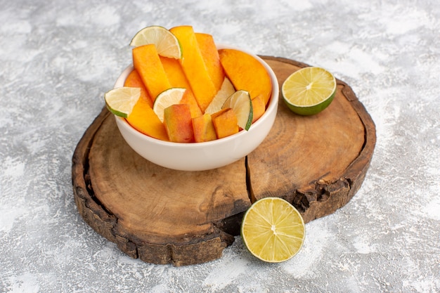 Front view sliced fresh peaches inside plate with lemons on the light white background.