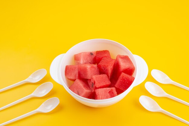 A front view sliced fresh watermelon inside white plastic plate on yellow desk