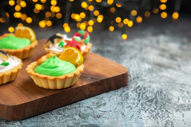 Front view small tarts on chopping board xmas ornaments on dark surface xmas lights