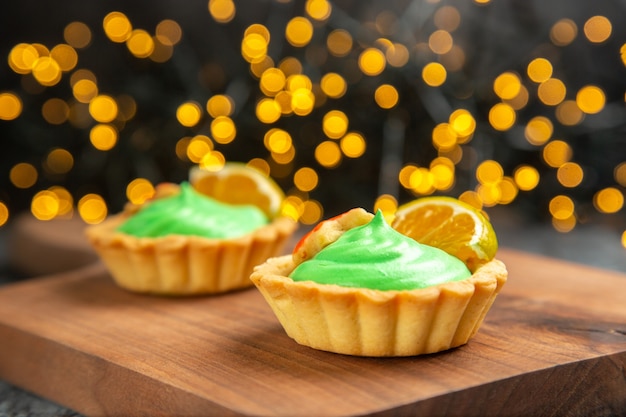 Free photo front view small tarts on cutting board on dark surface xmas lights