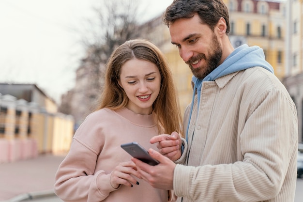 Free Photo front view of smiley couple outdoors in the city using smartphone