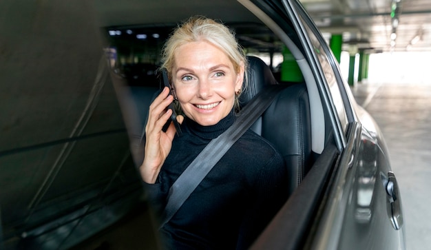 Front view of smiley elder business woman talking the phone in car