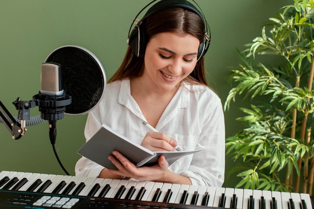 Front view of smiley female musician playing piano keyboard and writing songs while recording