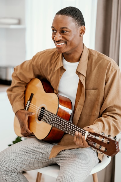 Front view of smiley male musician at home playing guitar