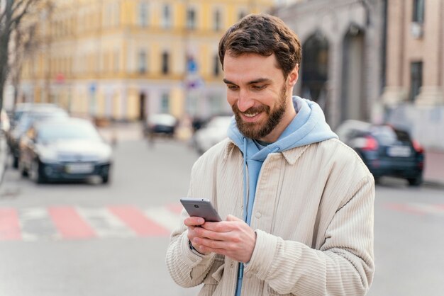 Front view of smiley man outdoors in the city using smartphone